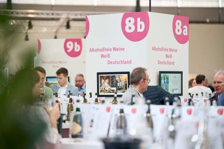 Besucher verkosten Weine und alkoholfreie Weine an einem Messestand mit klarer Kennzeichnung nach Sorten und Herkunft.
